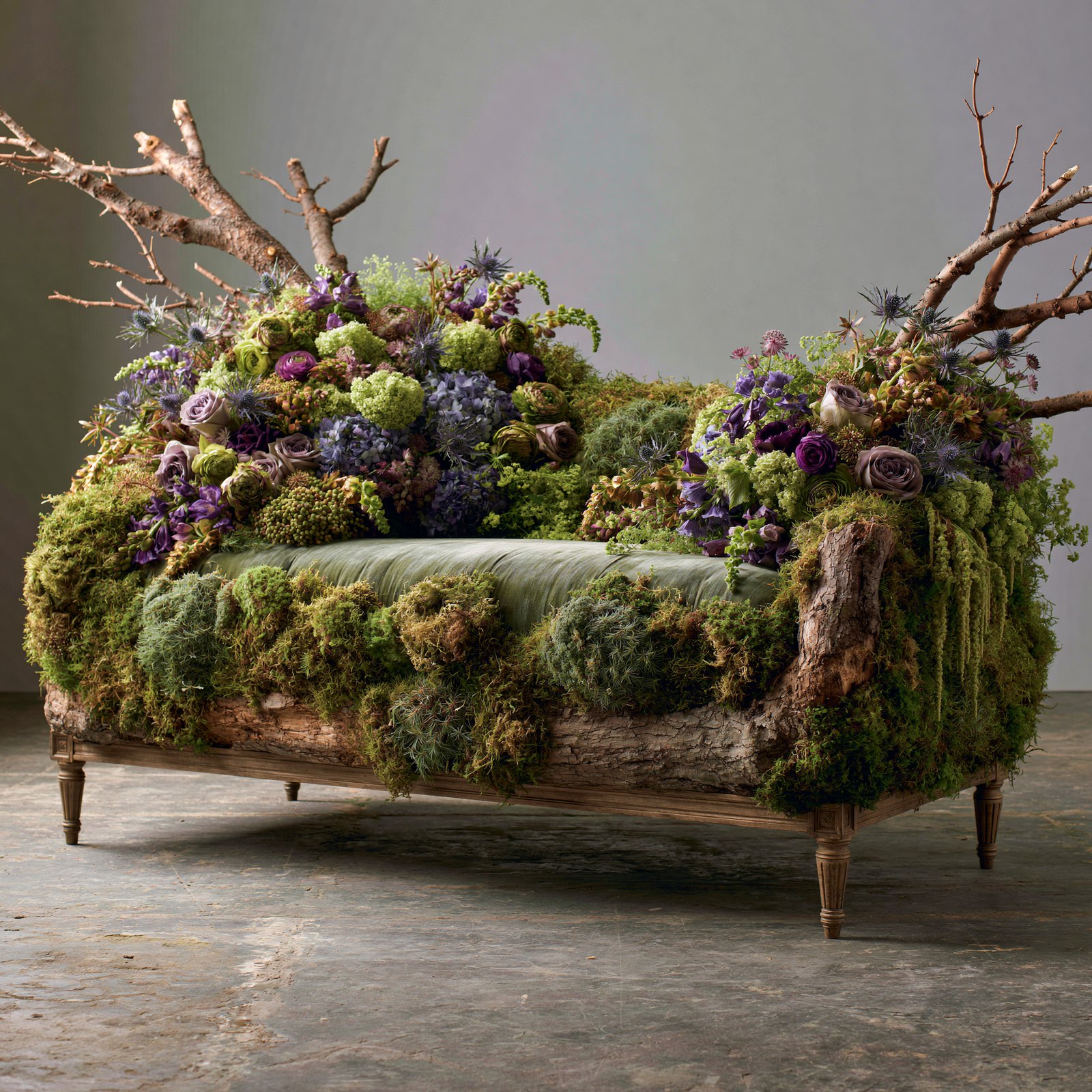 Daybed on a raw log frame with sage velvet cushion, moss, lavender roses and bare branches